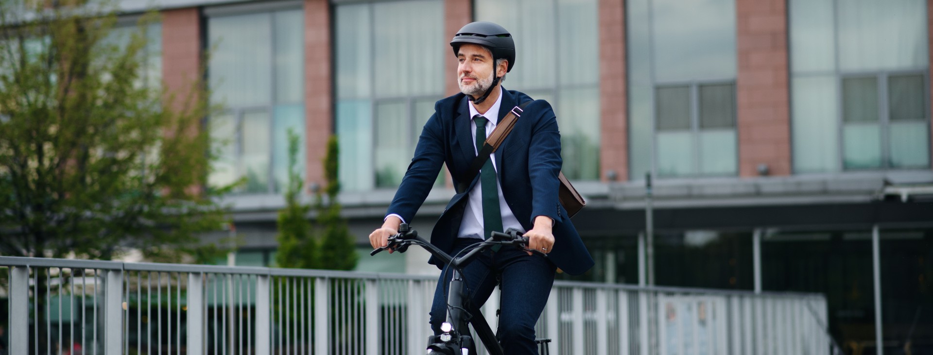 Mand i jakkesæt på cykel. Manden har cykelhjelm på og arbejdstaske over skulderen.