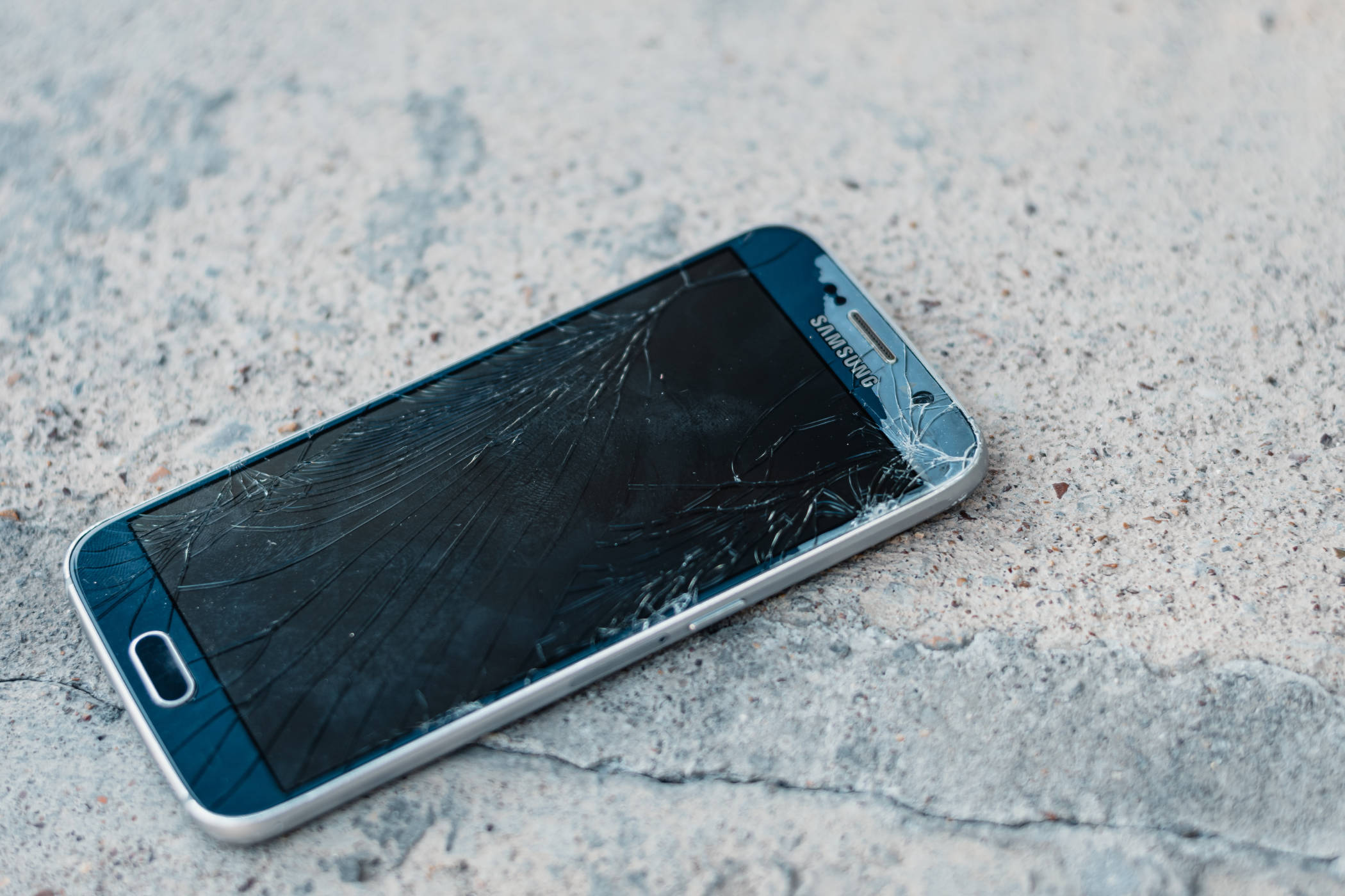 Samsung telefon med ødelagt skærm ligger på jorden.